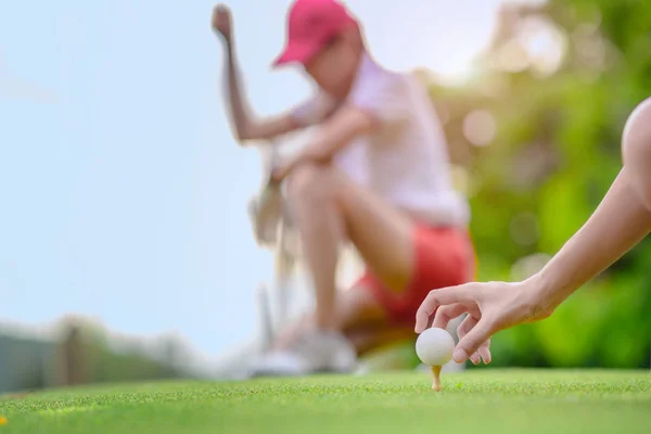 木製のティーに横たわってゴルフボールを保持若い女性のゴルフ選手の手 目的地のターゲットにボールを打つ準備と準備 背景で見て対戦相手やゴルフ仲間の仲間 — ストック写真