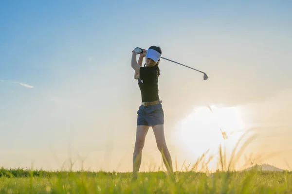 女高尔夫球手正在行动中 准备把高尔夫球从球道打到目的地 在日落时打到球道上 — 图库照片