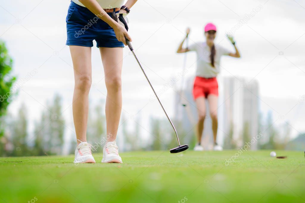 young woman golf player failed to putting golf ball into the hole on the green of the golf course, cheerfully and happiness on the failure of the opponent competitor in background 