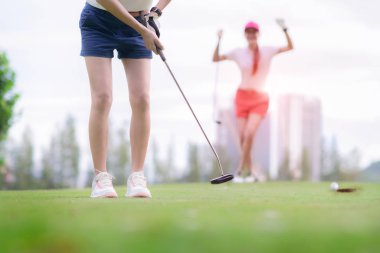 Genç bayan golfçü golf sahasının yeşilindeki deliğe atmayı başaramadı, neşeyle ve arka plandaki rakibinin başarısızlığıyla mutlulukla. 