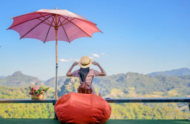 Kafenin terasında oturan kadın gezgin kırsal kesimdeki dağın manzarasının tadını çıkarıyor, keyifli bir hayat sürüyor.