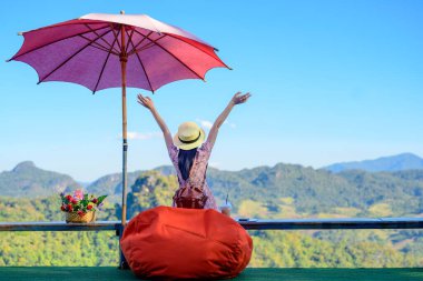 Kafenin terasında oturan kadın gezgin kırsal kesimdeki dağın manzarasının tadını çıkarıyor, keyifli bir hayat sürüyor.