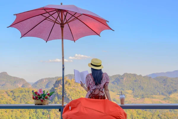 Kadın gezgin rahat bir şekilde terasta oturur, sabah kitap okur, yaz tatilinde seyahat eder, seyahatin tadını çıkarır ve hareketli bir şekilde dinlenir.,