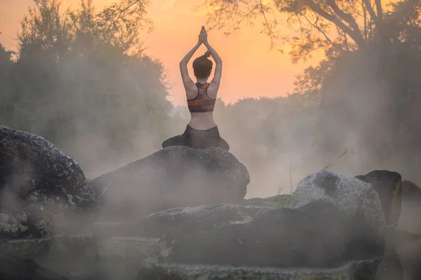 young woman in action of yoga practice in steaming hot spring water, the nature yoga exercise in hot spring steaming water at morning sunrise