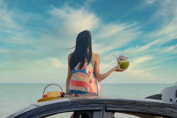 女人高高兴兴地坐在车顶上 手里拿着新鲜的椰子水果 夏天和度假在海滨 — 图库照片