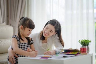 Modern anne, ev ödevlerine kızıyla birlikte katılıyor, evde mutlu vakit geçiriyor ve rahat hissediyor.