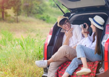 Çift aşığı arabanın arka kapağında oturuyor, yolculukta fotoğraf çekmenin keyfini çıkarıyor.