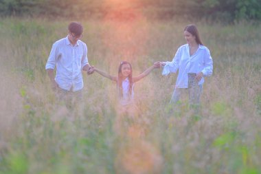 Bir grup sıcak aile, gün doğumunda kır çiçeklerinin olduğu çayır tarlasında birlikte oynamanın keyfini çıkarırlar. 