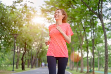 Genç Asyalı kadın şehir parkında koşu yaparak egzersiz yapıyor.