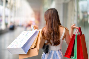 Mutlu kadın ve alışveriş merkezinde neşeli, alışveriş ve alışveriş tüketiciliği iki elinde de bir sürü torba tutuyor.