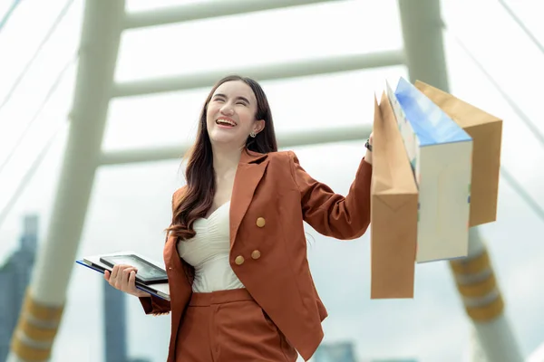 happy business woman joyful in shopping mall center, cheerfully buying and shopping consumerism with many bags holding in hands