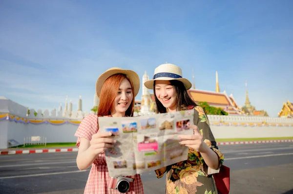 tourist women looking map guide with talking discussion find location visit on the palace temple in Bangkok of Thailand, Emerald Buddha Temple, Wat Phra Kaew, Royal Palace popular tourist place