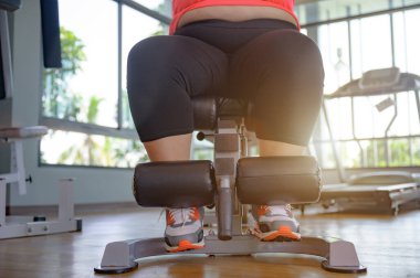Tombul şişman kadının bacakları spor salonunda ağırlık kaldırarak spor yapmaya çalışıyor.