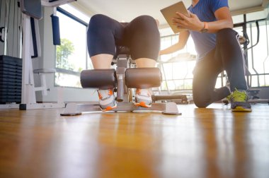 Egzersiz yaparken tombul şişman bir kadının bacakları, rekor seviyede aktiviteleri olan koç veya antrenörün bakımını ve müdahalesini üstlenir.