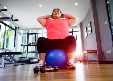 Spor salonunda topun üzerinde oturan tombul şişman kadın.