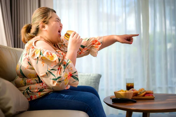 plump fatty woman hunger enjoy eating a lot junk food with high calories while watching entertainment TV in living room