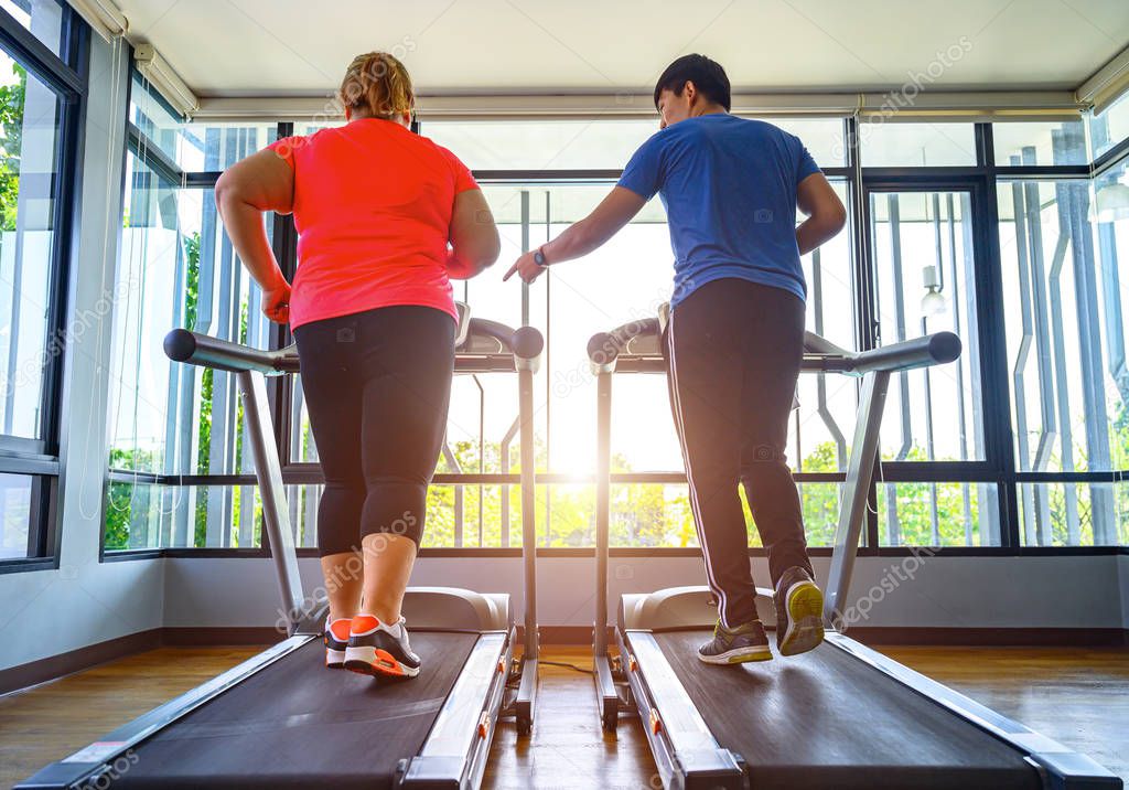 man trainer coach and fat woman being run or jog on belt of treadmill machine, workout under instruction of personal coach