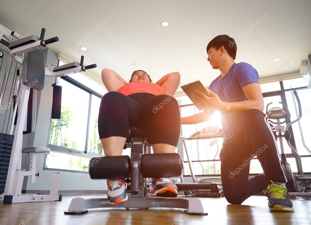 plump fat woman in action of exercise under takes care and intruction of coach or trainer with record activities on device