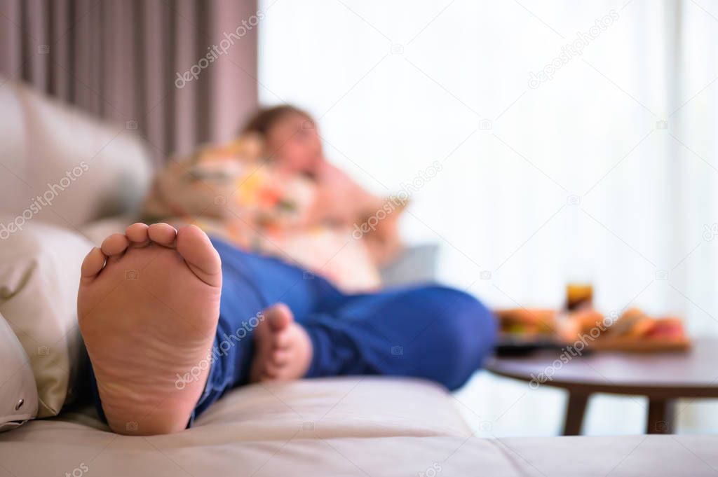 large foot of woman laying lazy while eating junk food in living room 