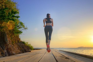 healthy slim woman jogging alone at daily morning on the wooden jetty bridge or pier, daily exercise workout running at light of sunset, trail competition at sea
