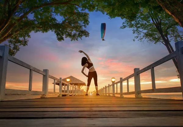 Sportlerin Beim Üben Auf Holzbrücke Bei Sonnenuntergang Mit Motorparaguide Über — Stockfoto