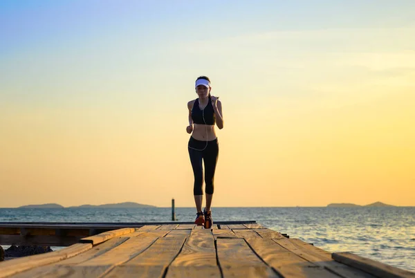 sport woman in running trail on wooden bridge at sunset, enjoy music while workout on the pier jetty in the sea