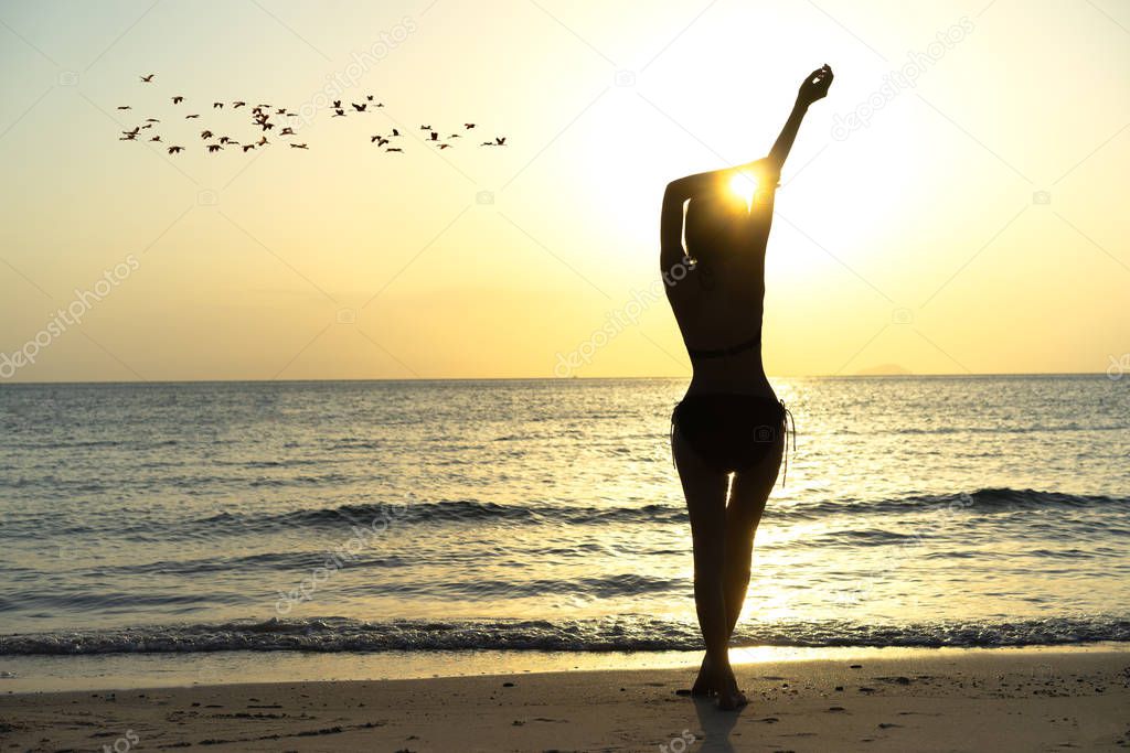Silhouette slim woman standing on the sea beach enjoy sunset alone, comfrotable and relax on the summertime vacation and holiday