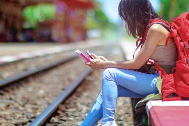 asian young woman checking train schedule online by mobile phone, or chating social online during waiting for the next train, waste time activity in trip waiting