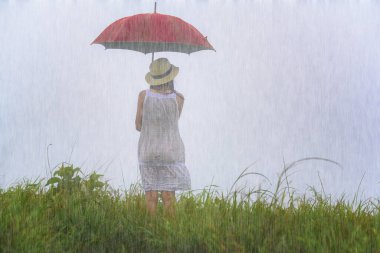 woman holding red umbrella standing in the raining at meadow field, stand alone emotion in the rain storm