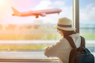 woman passenger or traveler tourist looking at watch on hand, in worry of the flight schedule in late or delay, sitting upset in the transit hall of the airport waiting for aircraft