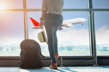 Kadın turist ya da yolcu, havaalanı terminalinin transit koridorunda duruyor, yurtdışına gitmek için uçak kalkışını bekliyor, arka plandaki uçuş uçağının inişini bekliyor.
