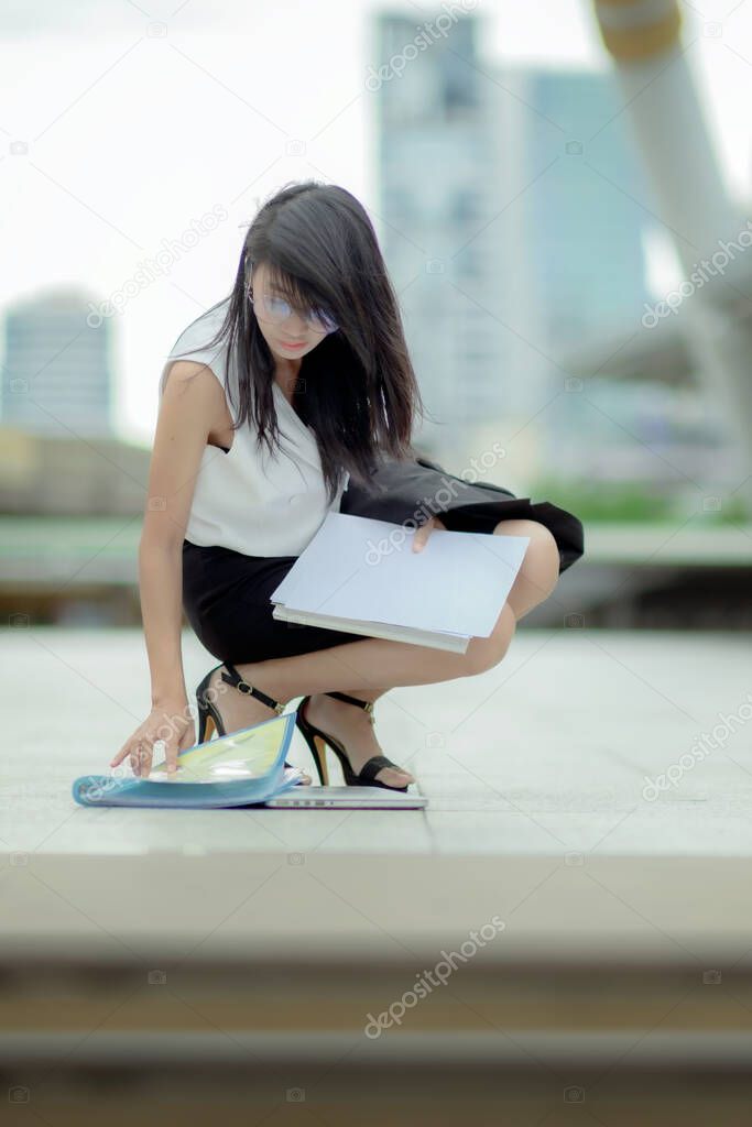 working office woman in busy motion at rush hours by drop documents paper to the floor in public place, sitting to collect dropped paper in working rush hours