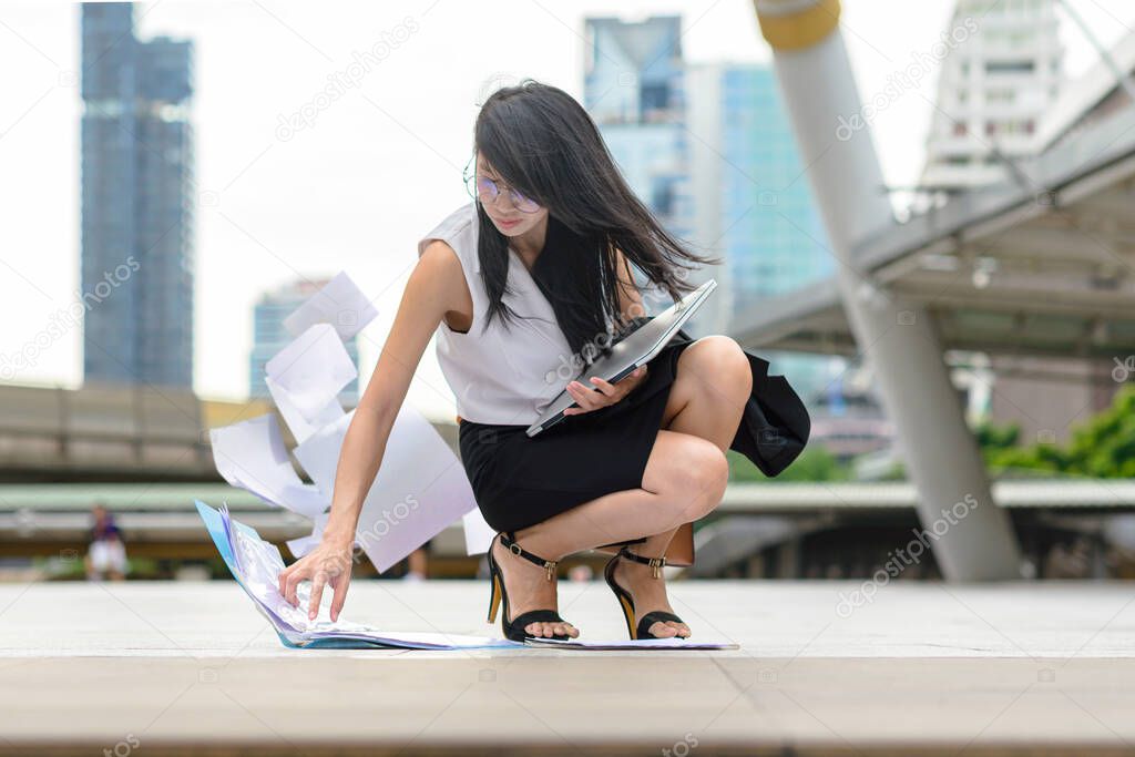 working office woman in busy motion at rush hours by drop documents paper to the floor in public place, sitting to collect dropped paper in working rush hour