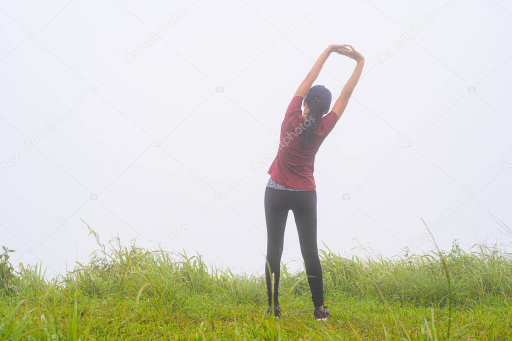 young woman in an action of pre-practice exercise doing in the morning of mist full around the meadow area