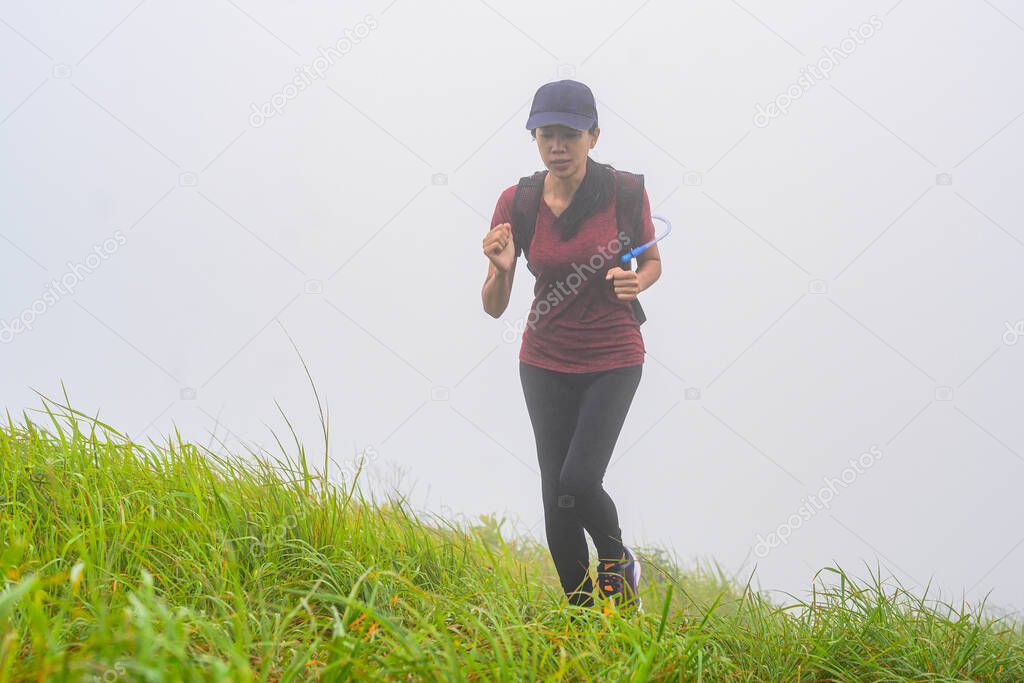 sporty woman running trail competition upon the hill mountain in the morning, with mist are full around the meadow area of the hil