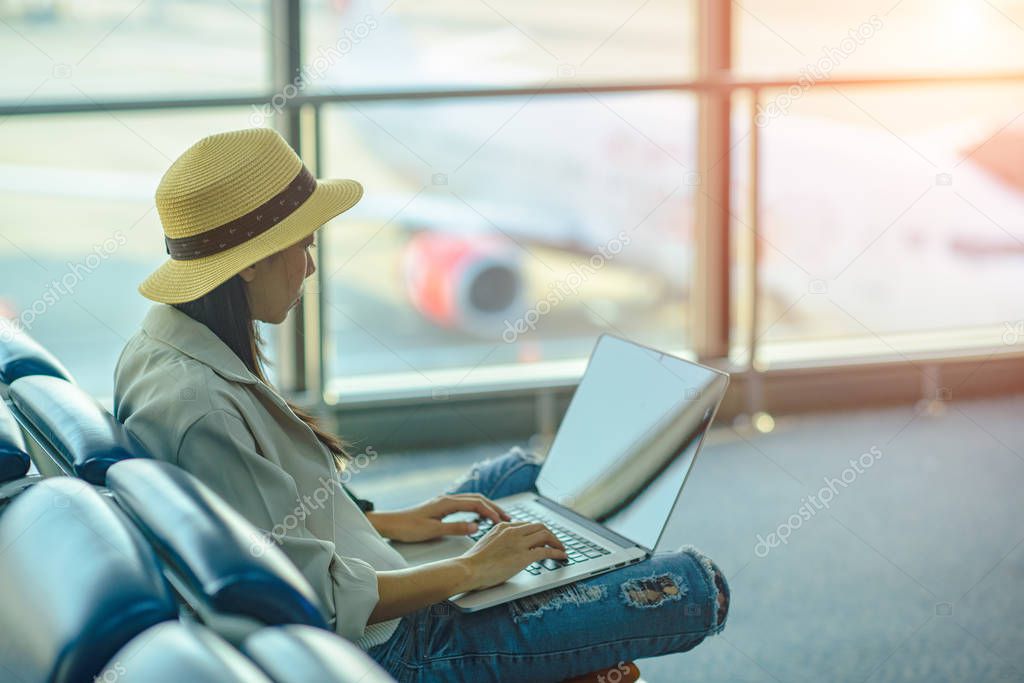woman passenger or traveler tourist looking at computor for next schedult of the flight, in worry of missing flight, sitting upset in the transit hall of the airport waiting for next aircraft lis