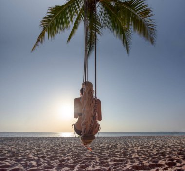 Deniz sahilinde, tahta salıncakta oturan bir kadın. Sıkıcı ve üzgün. Gün batımını görüyor musun?