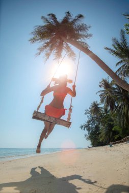 Kadın eğleniyor ve sallanıyor hindistan cevizi palmiyesinin altında, deniz kenarında, güneş ışığı ve günbatımı ışığı rahat ve rahat
