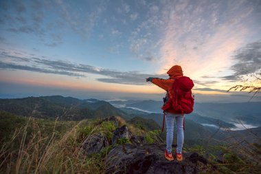 Sırt çantalı kadın turist, dağların arasında sisin ve sisin doğasının tadını çıkarıyor. Vahşi doğada tek başına seyahat ediyor. Dağların zirvesinde yürüyüş yapıyor.