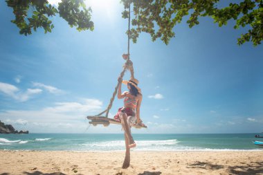 woman enjoy happy the nature of the sea beach by sitting on the wooden swing tie under the shadow of the plam tree, long weekend and vacation holidays spent slow life on the beach - Image