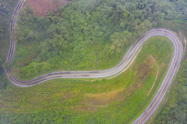 aerial top view of sharp curve of high way road in mountain at countryside. develop new road along to the forest