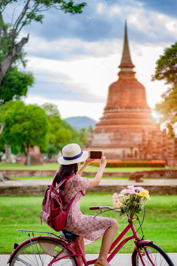 woman tourist enjoy riding vintage bicycle to see the historic park of Thailand, exciting taking photo to the wonderful place of sightseeing