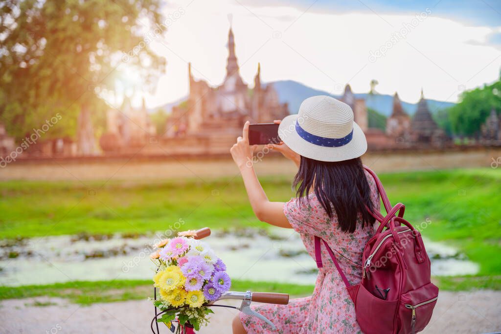 woman tourist enjoy riding vintage bicycle to see the historic park of Thailand, exciting taking photo to the wonderful place of sightseein