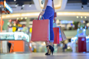 Alışveriş merkezinde mutlu ve neşeli narin bir kadının elindeki alışveriş torbaları, iki elinde de bir sürü torba bulunan alışveriş ve alışveriş tüketimi.