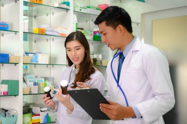 Kadın eczacı ve doktor, eczanede birlikte çalışarak stoklarda kalan ilaç veya denge listelerini kontrol ediyorlar.
