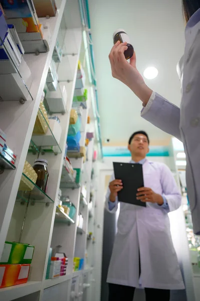 hand of woman holding bottle of medicine in pharmacy drug store, checking inventory list and product quality of the medicine
