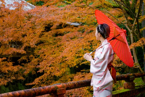 Geleneksel ya da orijinal Japon tarzı giyinen bir kadın, köy köprüsünde yürüyor, eski bir Japon tarzı, sonbahar mevsimi değişiyor, Japonya 'ya turist ziyareti için popüler ve ünlü bir yerde çiçek açıyor.