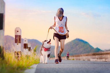 Kadın köpek yavrusuyla günlük egzersiz yapıyor, parktaki yolda koşuyor. 