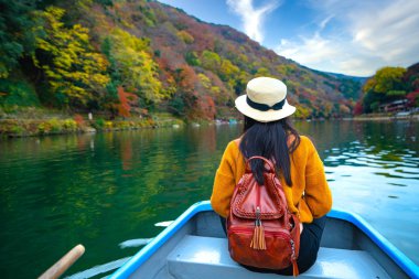 Kadın gezgin turist, sonbahar mevsiminde turistlerin ünlü ve popüler yeri olan Arashiyama nehrinde keyifli bir hayat sürüyor.