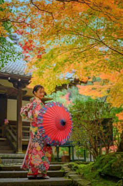 Geleneksel kimono tarzı retro şemsiyeli kadın, sonbaharda köyün bahçesinin ortasında tek başına duruyor, Japonya 'ya geliyor spor müsabakalarında seyahat ediyor ve ziyaret ediyor.